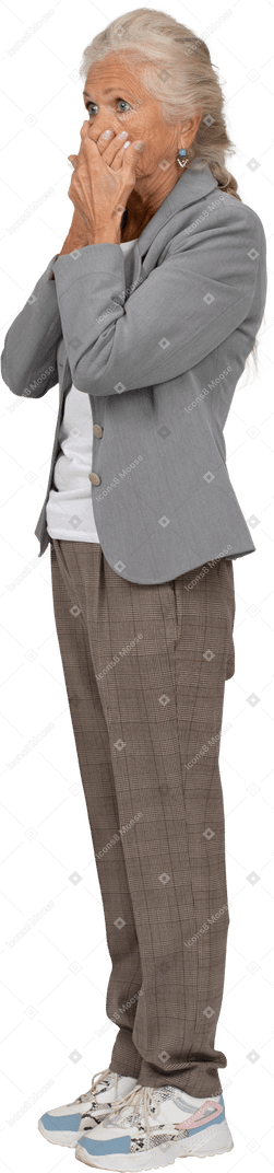Side view of a scared old lady in suit covering mouth with hands