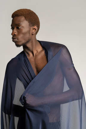 Front view of a young afro man holding a shawl on his shoulders and looking aside