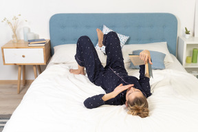 Full-length of a bored young lady trying to read book in bed