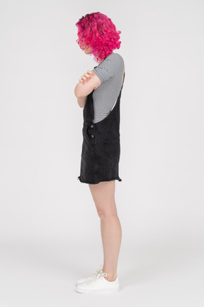 Pink haired girl standing in profile with her arms folded