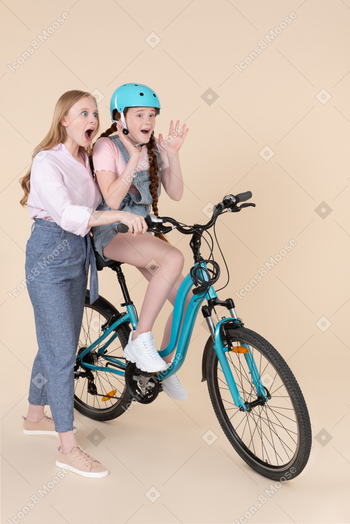 Surprised young woman teaching scared teenage girl how to ride the bicycle