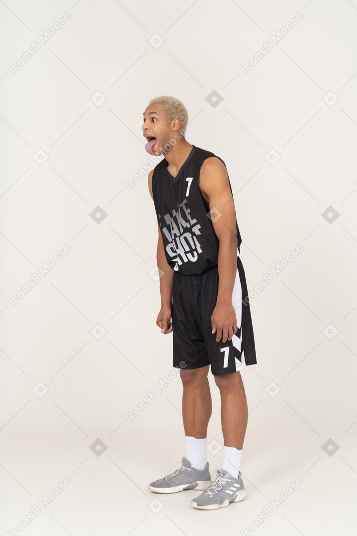 Vista di tre quarti di un giovane giocatore di basket maschio pazzo che mostra la lingua