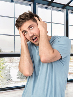 A man holding his head in front of a window