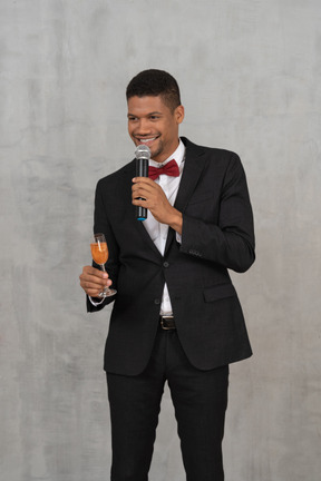 Молодой человек держит бокал шампанского и микрофон и смотрит в сторону