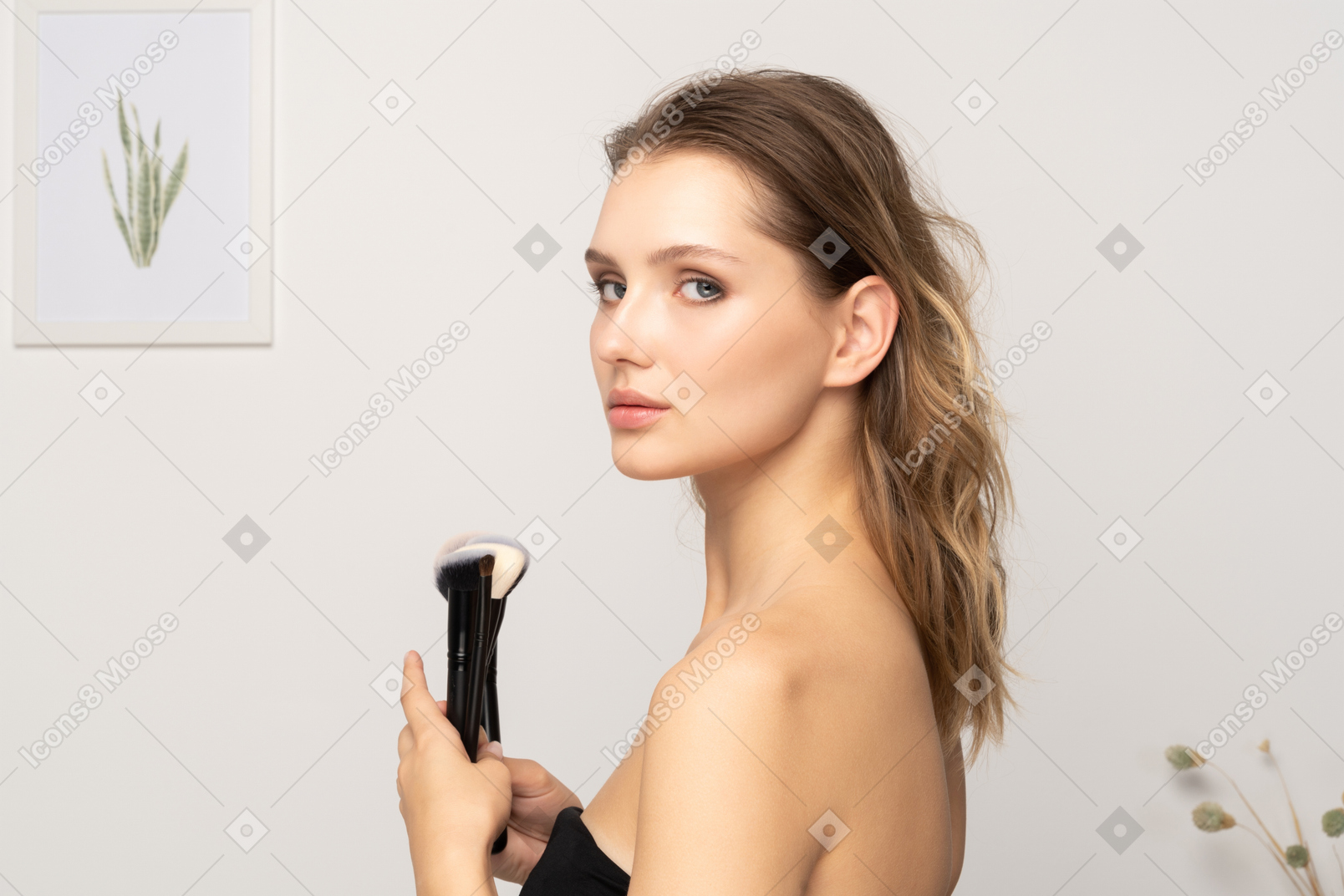 Vue latérale d'une jeune femme sensuelle tenant des pinceaux de maquillage