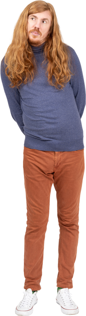 Vista frontal de un joven con ropa informal de pie con las manos detrás de la espalda