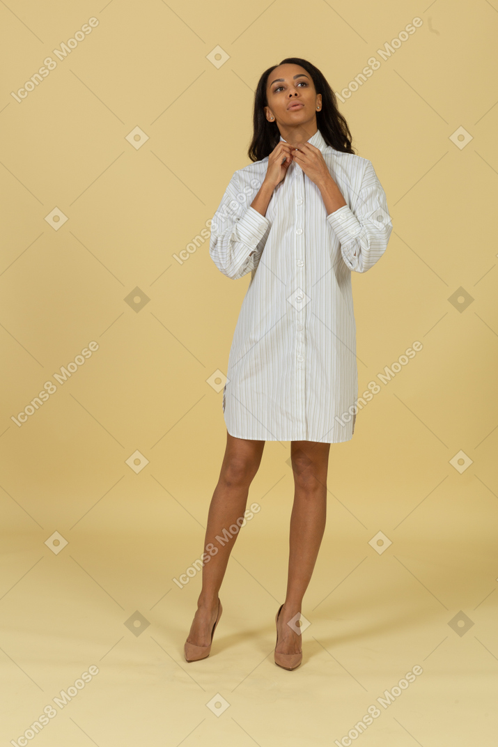그녀의 칼라를 조정하는 흰 드레스에 어두운 피부의 젊은 여성의 전면보기