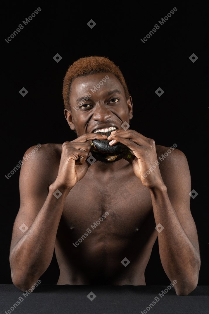 Vista frontal de um jovem afro mordendo um hambúrguer