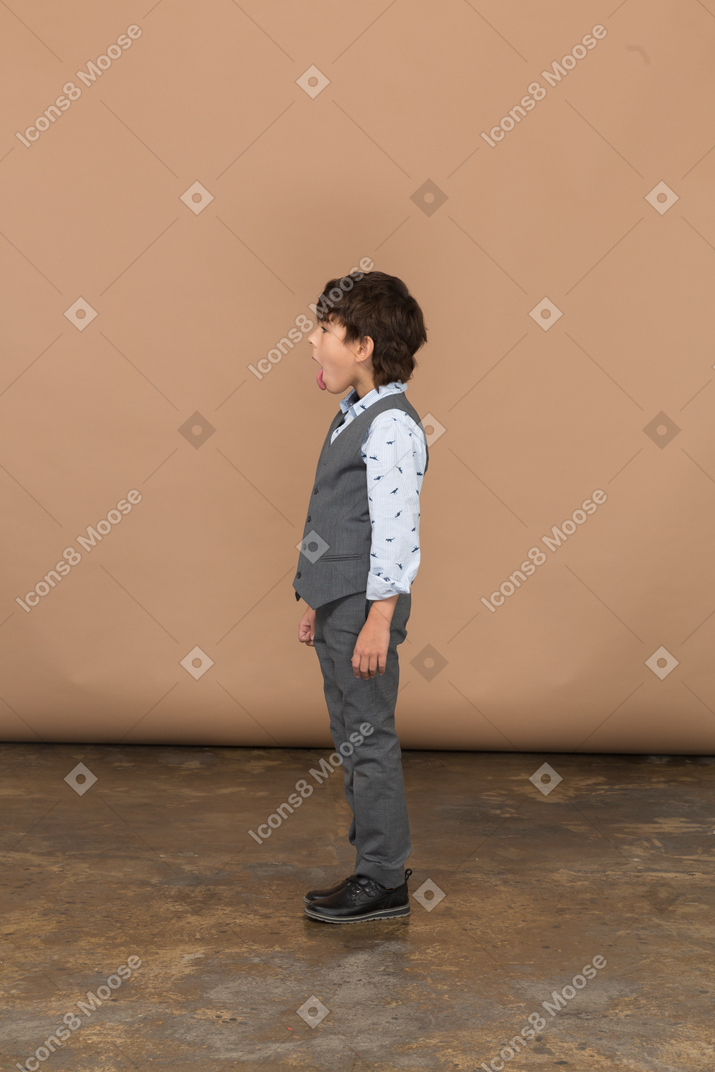 Вид сбоку на мальчика в сером костюме, показывающего язык
