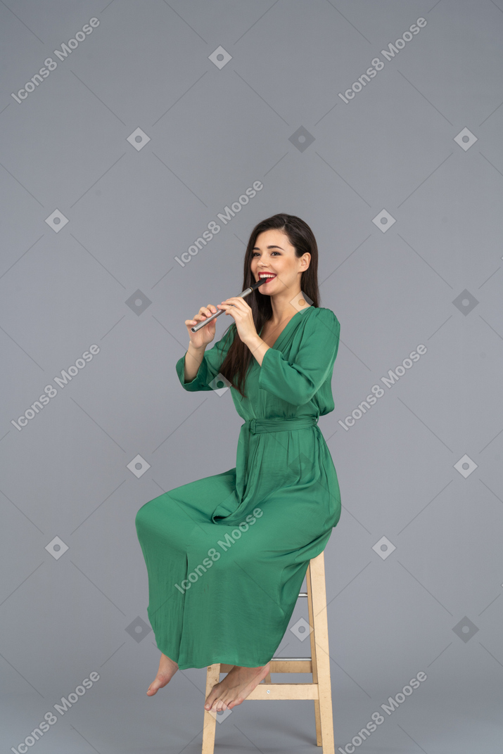 全长的微笑的年轻女士，穿着绿色的衣服，坐在椅子上，一边演奏单簧管