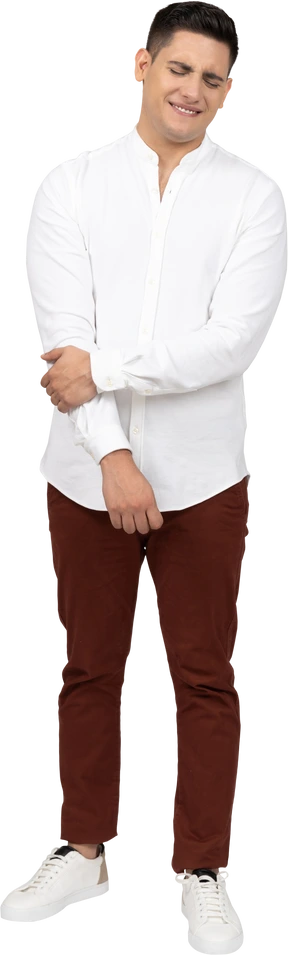 Front view of a young latino man holding his arm and closing eyes in disgust with a smile