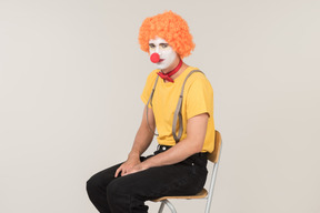 Male clown in red wig sitting on the chair