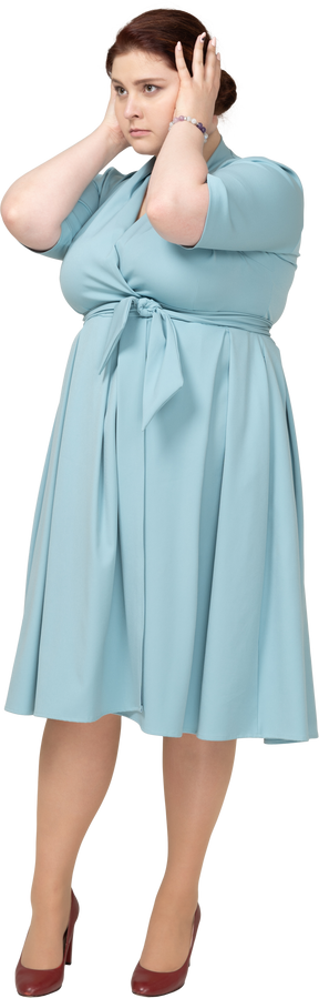 Vista frontal de una mujer en vestido azul cubriendo las orejas con las manos