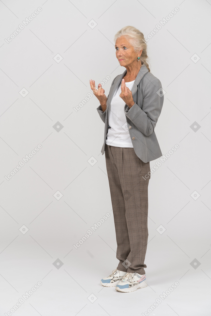 Вид сбоку на пожилую женщину в костюме, указывающую пальцами вверх