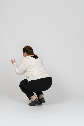 Rear view of a plump woman in casual clothes squatting