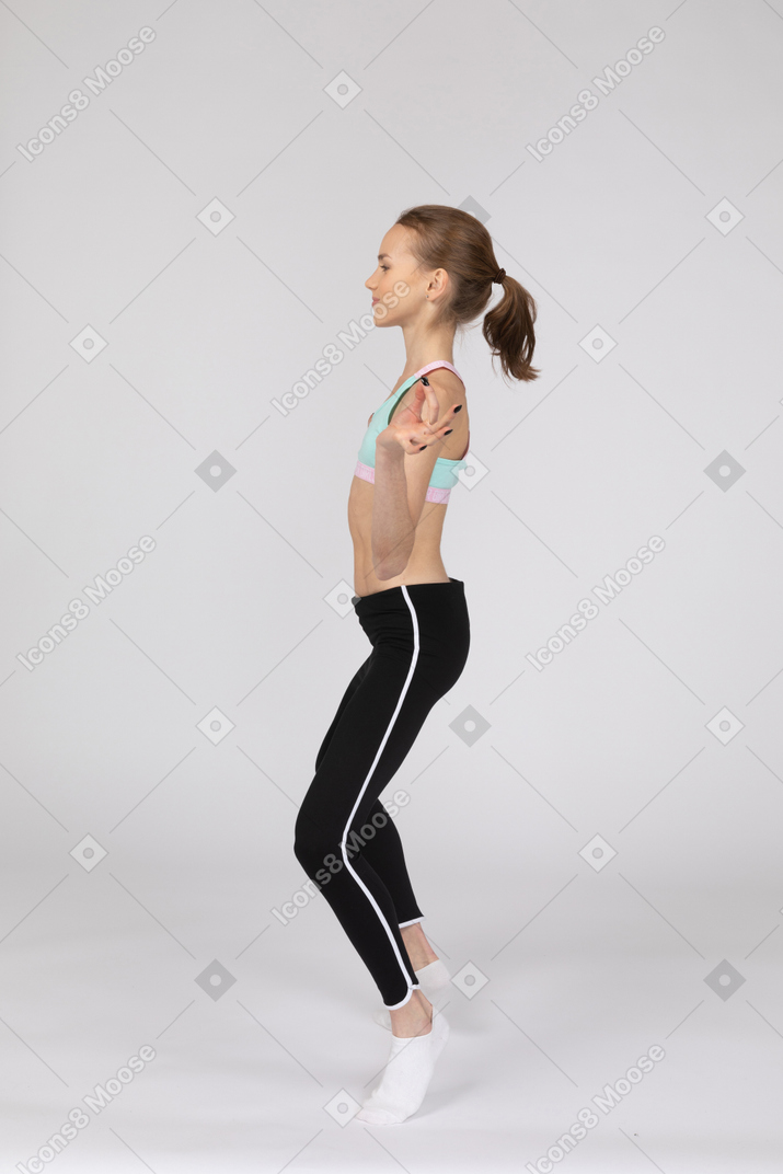Vista lateral de uma adolescente em roupas esportivas separando as pernas