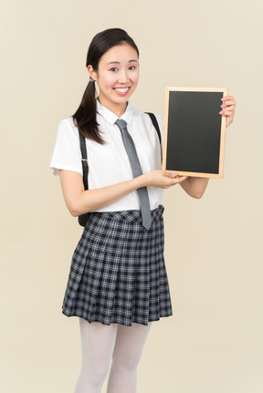 Ragazza asiatica sorridente della scuola che tiene piccola lavagna