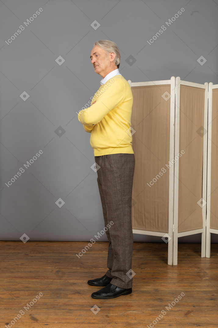 Vista lateral de un anciano curioso cruzando las manos y mirando a un lado