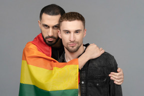 Front view of two young men half-hugging while wearing lgbt flag