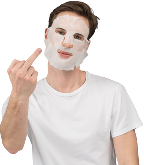 Front view of a young man in facial mask showing middle fingers