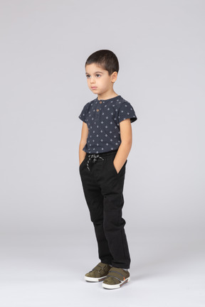 Vista frontal de un niño triste en ropa casual de pie con las manos en los bolsillos