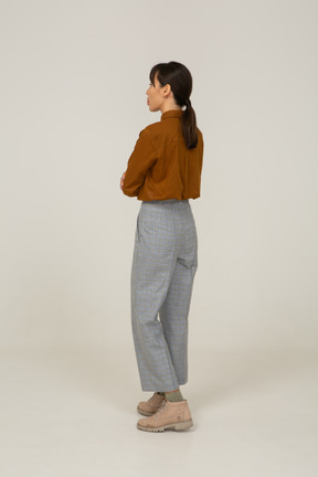 Vista posteriore di tre quarti di una giovane donna asiatica in calzoni e camicetta che incrocia le braccia e mostra la lingua