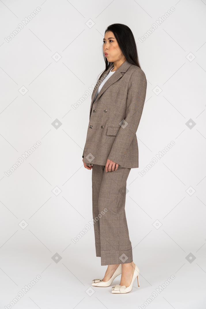 Vista de tres cuartos de una señorita en traje marrón soplando mejillas