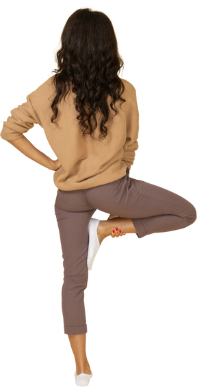 Vista traseira de uma jovem mulher de pele escura colocando a mão no quadril enquanto levanta a perna