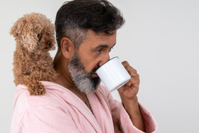 Reifer mann, der einen kaffee mit einem welpen auf seiner schulter trinkt