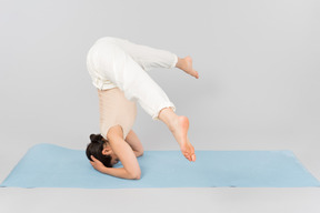 Mujer joven de pie sobre la cabeza en la estera de yoga