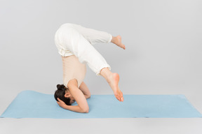 Jeune femme debout sur la tête sur un tapis de yoga