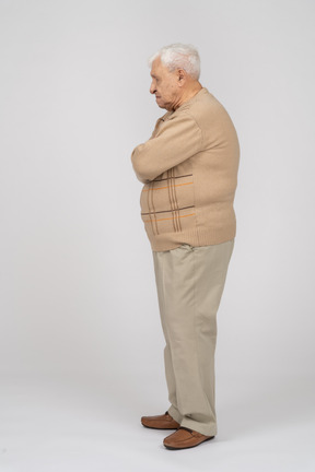 Side view of an old man in casual clothes standing with crossed arms