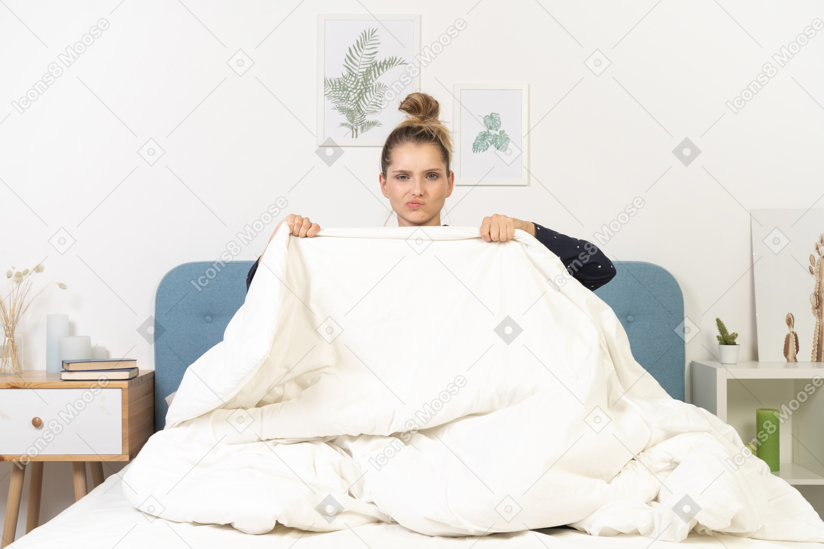 Front view of a grimacing young woman in pajamas hiding behind the blanket staying in bed
