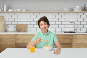 Boy sitting at a table with a bowl of cereal and a glass of orange juice