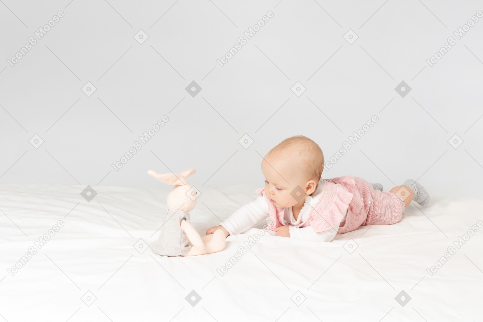 胃の上に横たわるとぬいぐるみを探している女の赤ちゃん
