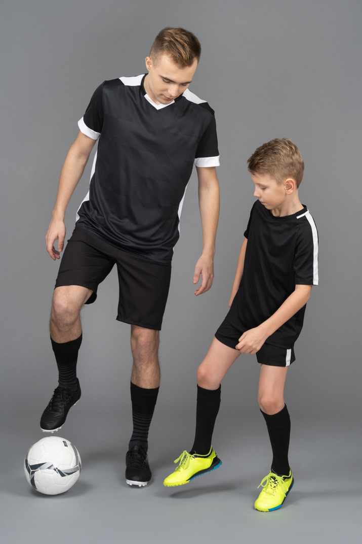 Full-length of a young man coaching little boy how to play fooyball