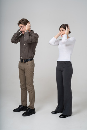 Vista de tres cuartos de una pareja joven en ropa de oficina tocando la cabeza