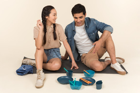 Interracial couple sitting on karimat near dishes