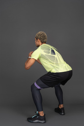 Three-quarter back view of a dark-skinned young man squatting with an elastic rubber