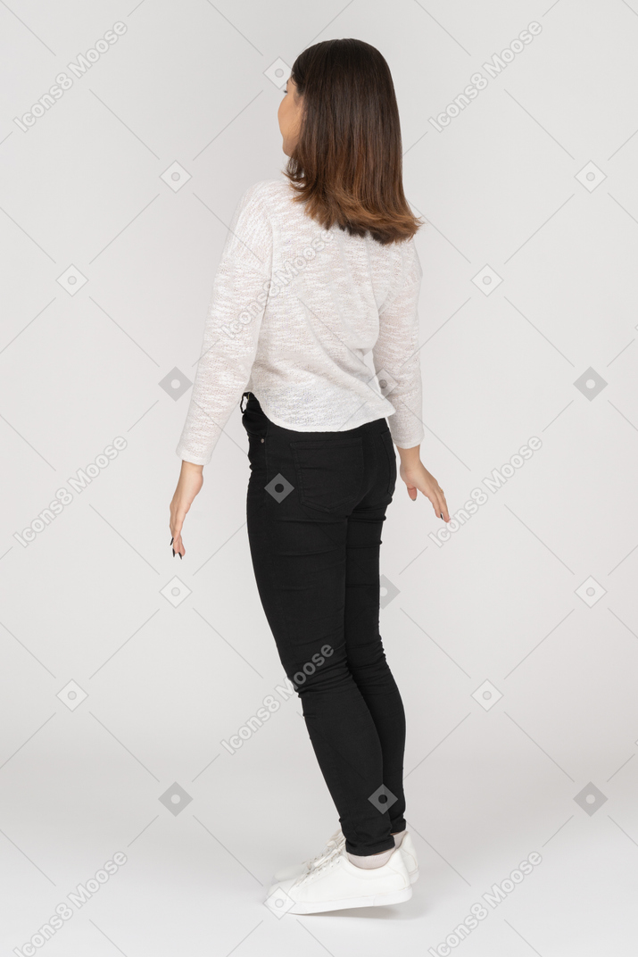 Three-quarter back view of a young indian female in casual clothes outspreading hands