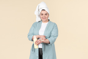 Young plus-size girl in a blue bathrobe taking care of her skin after a shower