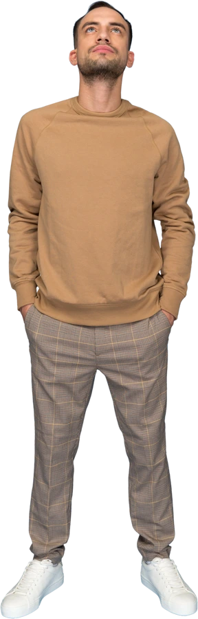 Young man standing with hands in pockets and looking up