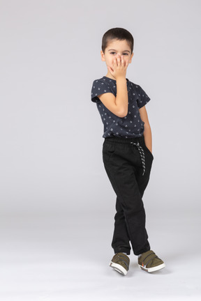 Вид спереди симпатичного мальчика в повседневной одежде, прикрывающего рот рукой