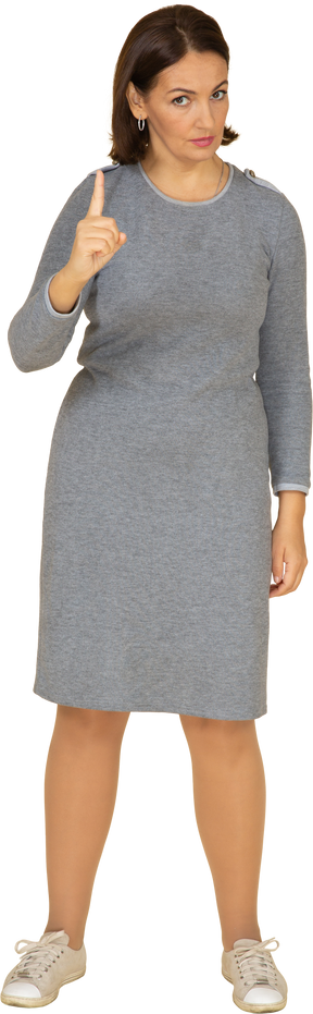 Vista frontal de una mujer en vestido gris apuntando hacia arriba con un dedo