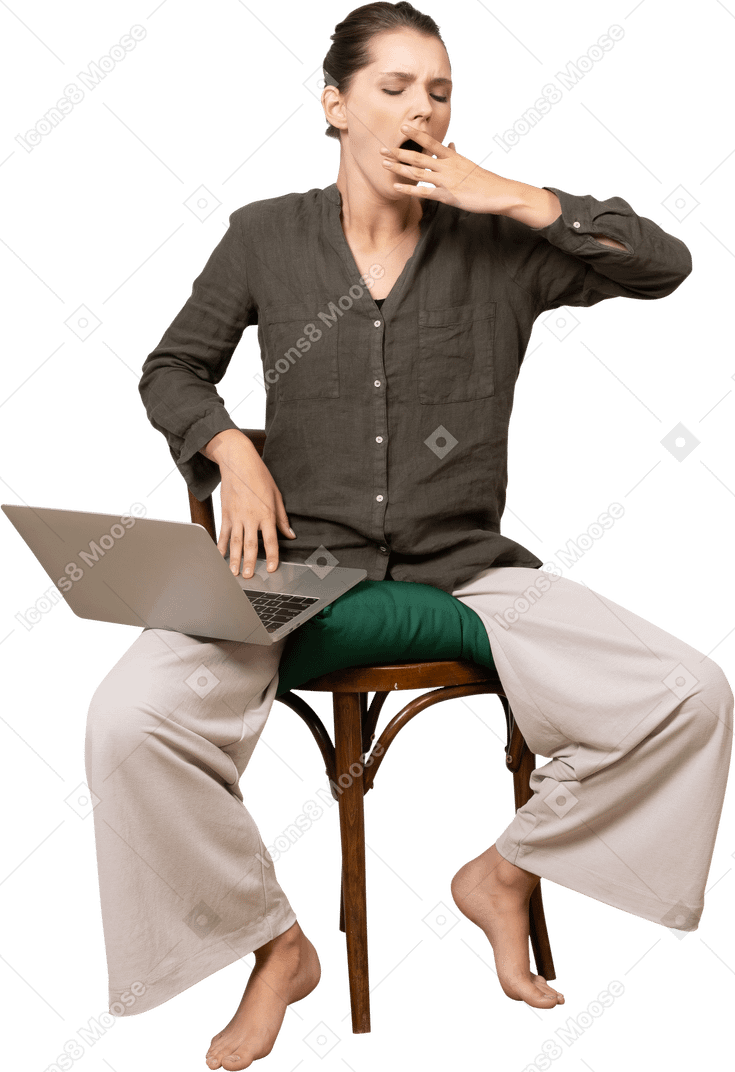 Front view of a tired young woman wearing home clothes sitting on a chair with a laptop