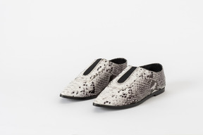 A three-quarter front shot of a pair of white & black snakeskin flat shoes