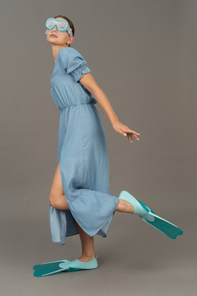 戴着浮潜面罩和脚蹼站在一条腿上的年轻女子的侧视图