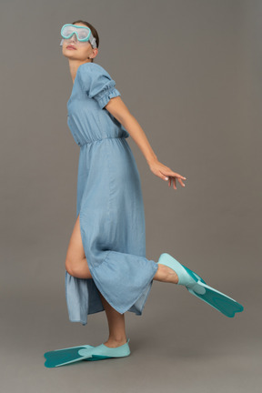 Side view of young woman standing on one leg in snorkelling mask and flippers