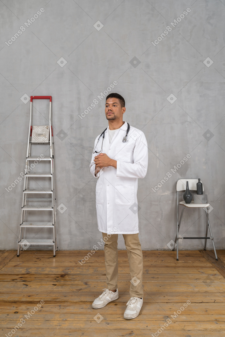 Vista de três quartos de um jovem médico em uma sala com escada e cadeira de mãos dadas