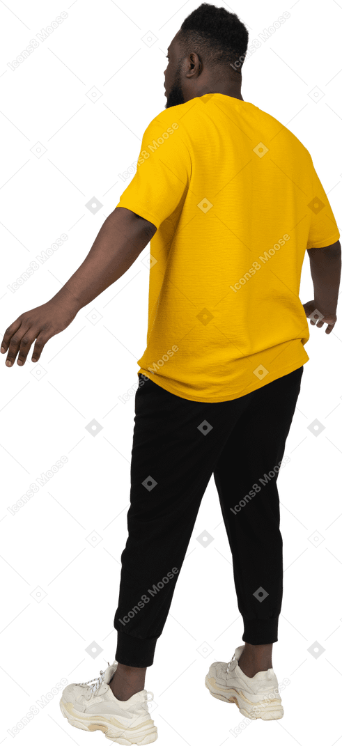 腕を広げている黄色のtシャツを着たショックを受けた若い浅黒い肌の男の4分の3の背面図